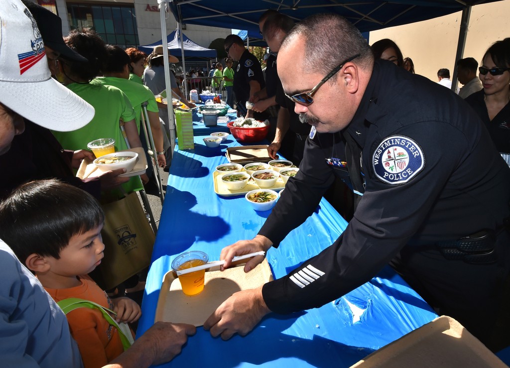 Westminster PD Cmdr. Mike Chapman helps serve a free meal that includes a drink and Pho (a type of Vietnamese soup) during the Viet-CARE Pho-Covery Celebration at the Asian Garden Mall in Westminster. Photo by Steven Georges/Behind the Badge OC