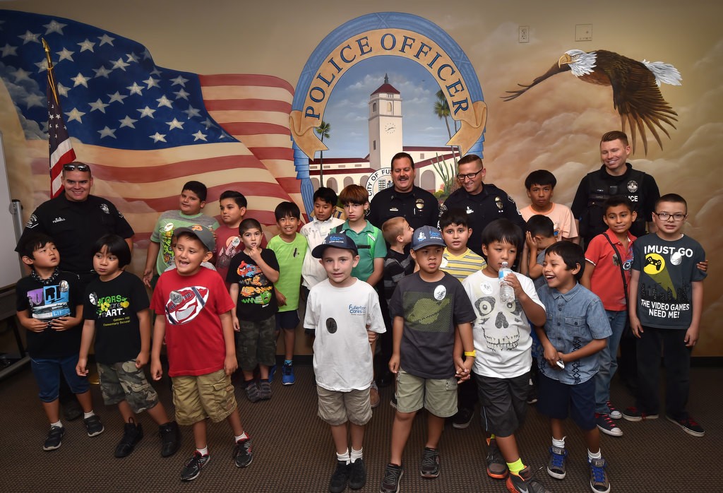 Fullerton Police officers Jonathan Ferrell, back left, Capt. Scott Rudisil, Sgt. Jon Radus and Officer Andrew Coyle stand with Autistic kids from Golden Hill Elementary School in the police briefing room during a tour of the Fullerton Police Station. Photo by Steven Georges/Behind the Badge OC