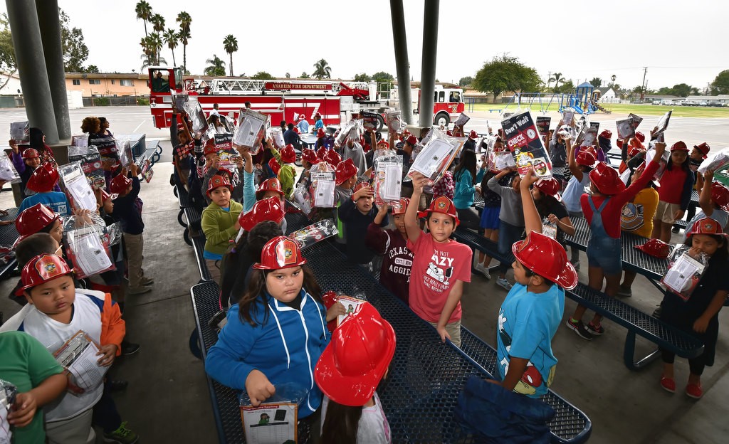 Kids from Edison Elementary School hold up their free smoke alarms and fire prevention education packets as Anaheim Fire & Rescue visits the Anaheim school for Fire Prevention Week. Photo by Steven Georges/Behind the Badge OC