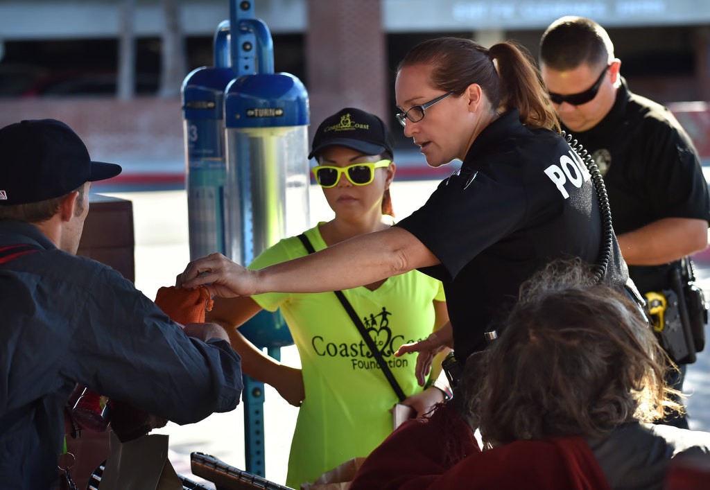 Fullerton PD Homeless Liaison Cpl. Ginny Johnson, with Coast to Coast Foundation founder Marie Avena next to her, helps hand out hygiene kits in orange bags during a visit to the OCTA Bus Stop in Fullerton. Photo by Steven Georges/Behind the Badge OC