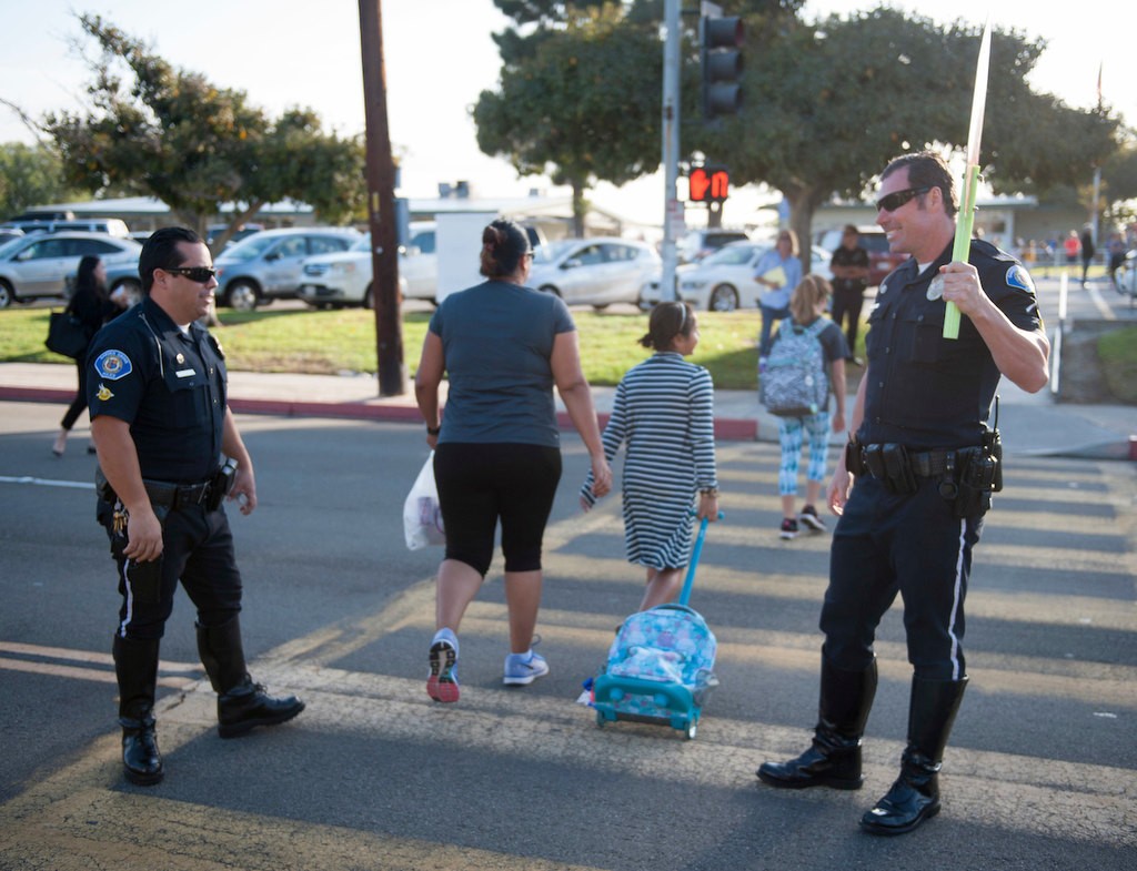 Garden Grove Police Officers Ronnie Reyes, left, and Tom Capps help students cross the street participating in National Walk to School Day in front of Enders Elementary before the start of class.