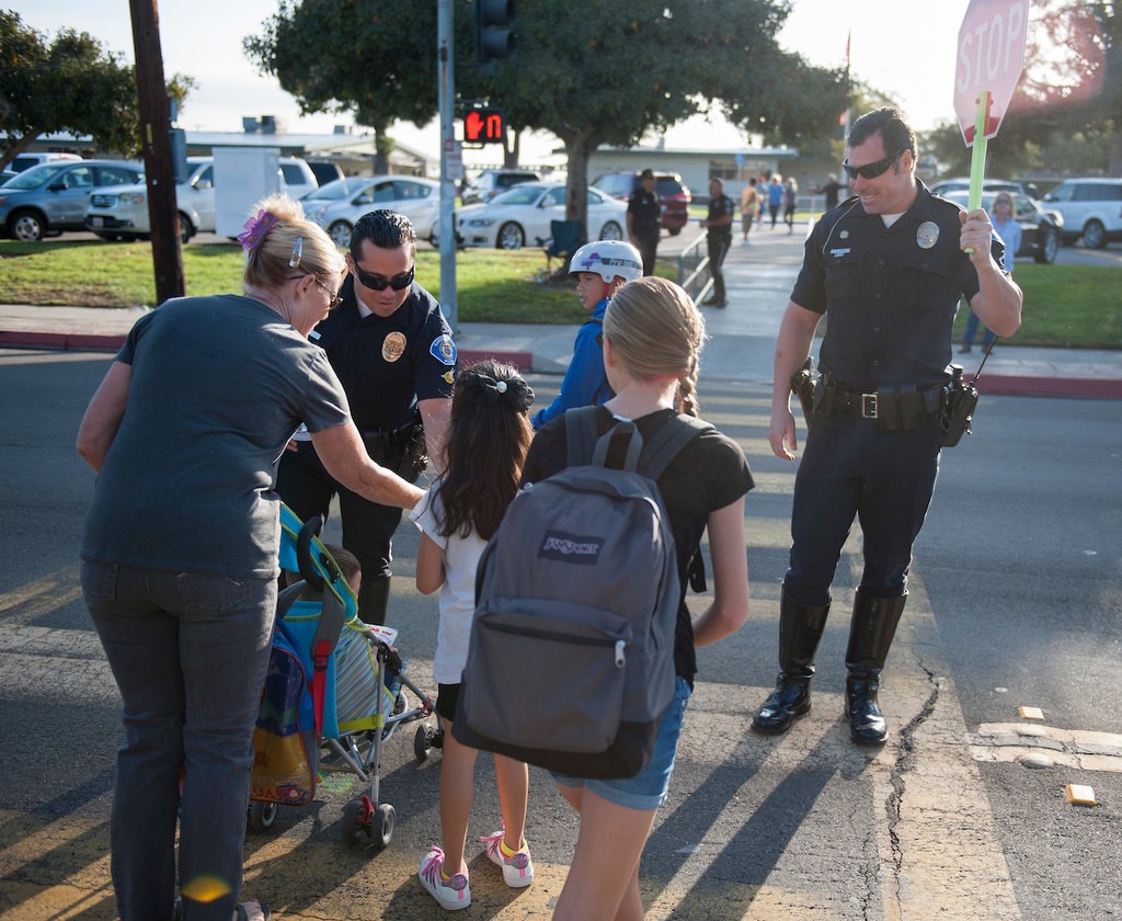 Garden Grove Police Officers Ronnie Reyes, left, and Tom Capps and out stickers and help students cross the street participating in National Walk to School Day in front of Enders Elementary before the start of class.