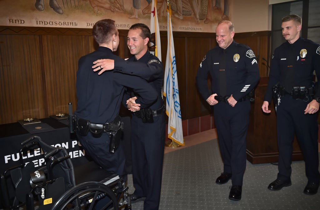Los Angeles PD Officer Nick Wiltz stands from his wheelchair as he gets a hug from Fullerton PD Officer Timothy Gibert during a visit to honor the three FPD officers who helped save his life. Behind them Cpl. Matt Wilkerson and Officer Michael Halverson, right. Officer Wiltz survived but lost a leg as a result of the motorcycle accident. Photo by Steven Georges/Behind the Badge OC