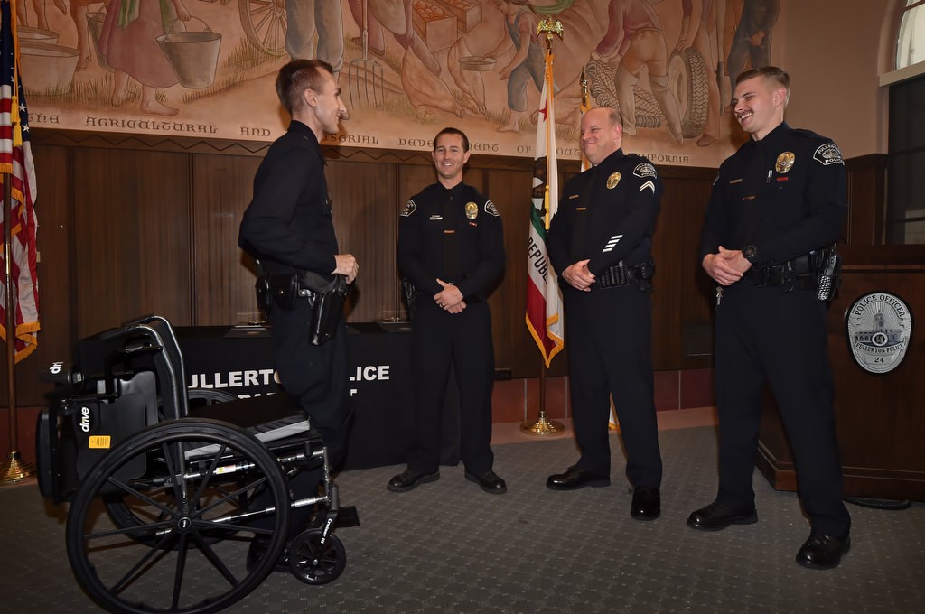 Los Angeles PD Officer Nick Wiltz, left, stands from his wheelchair to thank the three Fullerton PD officers, Timothy Gibert, Cpl. Matt Wilkerson and Michael Halverson, right, who helped save save his live during an off duty motorcycle accent in August. Photo by Steven Georges/Behind the Badge OC