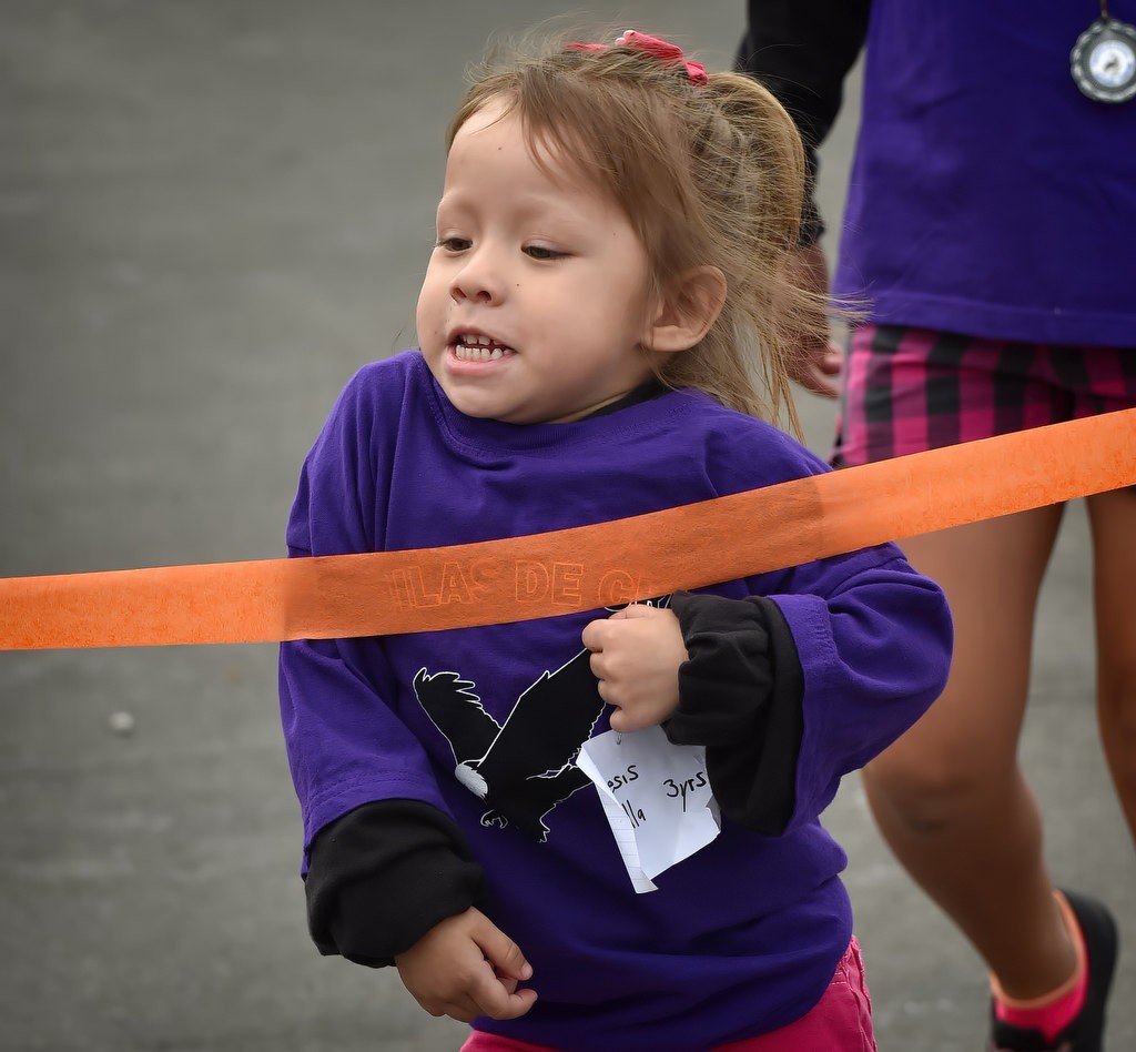 Genesis Estrellc, 3, runs through the finish line tape during a fun run for a community gathering at the Palma Vista Ave. neighborhood in Garden Grove. Photo by Steven Georges/Behind the Badge OC