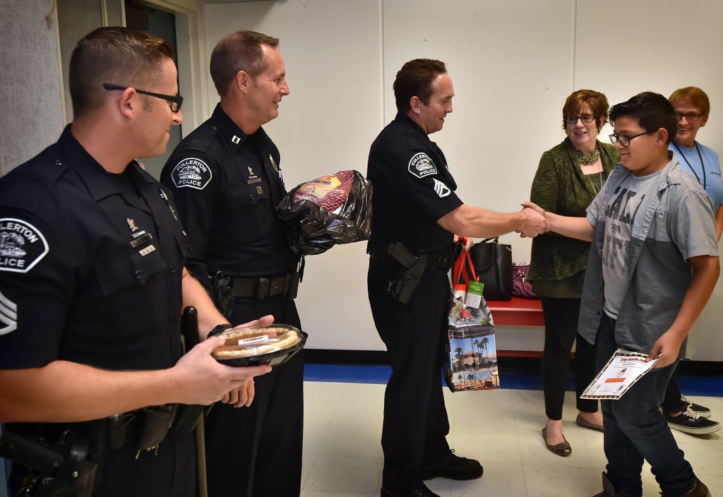 Ten-year-old Artie (Arturo) Diaz gets a hand shake from Anaheim PD Sgt. Joel Craft as Sgt. Jon Radus, left, and Capt. (and acting Chief) John Siko get ready to hand him his Thanksgiving food as part of GRIP’s Turkey Incentive at Valencia Park Elementary School. Photo by Steven Georges/Behind the Badge OC