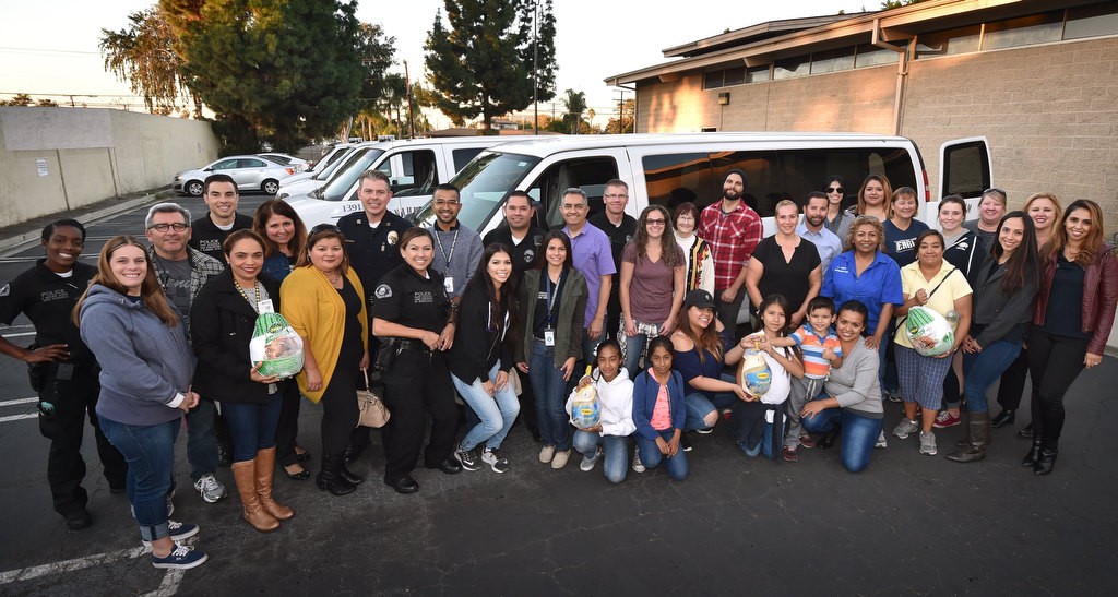 Representatives from Anaheim PD, Anaheim GRIP and school officials gather in front of white vans from Anaheim Public Works and Community Services to visit homes of Anaheim kids being honored by Anaheim GRIP and Anaheim Police with a turkey dinner. Photo by Steven Georges/Behind the Badge OC