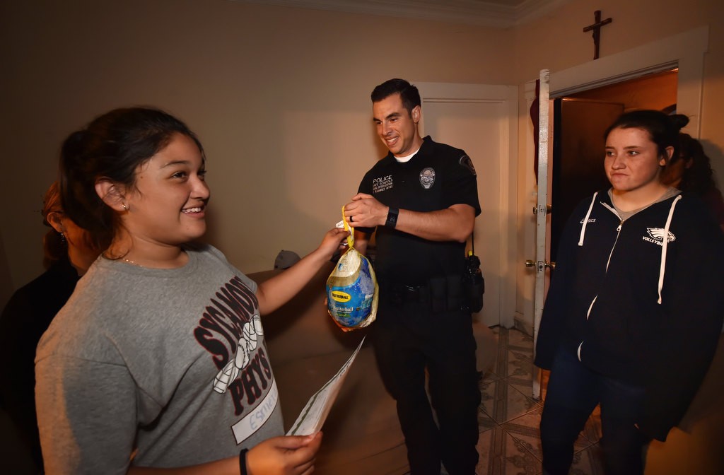 Esmeralda Vazquez, 12, is handed a turkey from Anaheim PD Officer Frank Ramirez as she and her family is brought a turkey dinner for her achievements. Photo by Steven Georges/Behind the Badge OC
