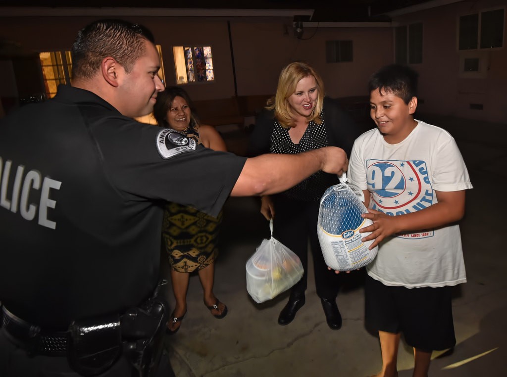 Jose Villalobos, 12, is handed a turkey by Anaheim PD Officer William Martinez as he and his family receives a full Thanksgiving dinner. Photo by Steven Georges/Behind the Badge OC