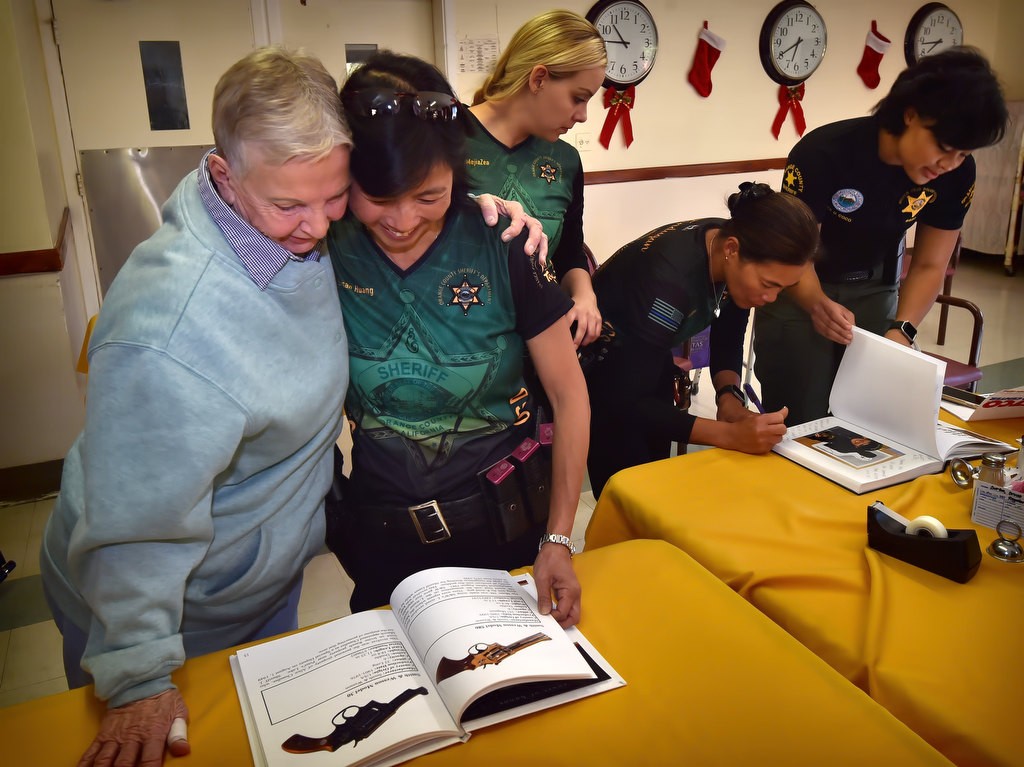 Alice Chandler gets a hug from OC Sheriff Dep. Susan Huang as they look through a book of historical guns that includes the gun Chandler uses as Orange County’s first female sheriff deputy. Photo by Steven Georges/Behind the Badge OC