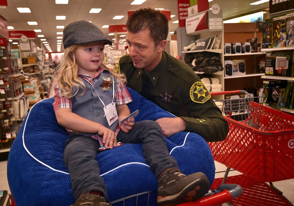 OC Sheriff’s Commander William Baker makes sure 4-year-old is comfy in his makeshift shopping cart chair as they head out for a Target store holiday shopping spree for the Shop with a Deputy event. Photo by Steven Georges/Behind the Badge OC