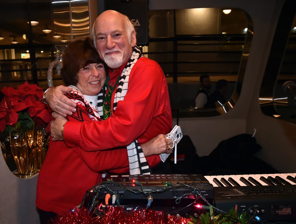 Lynda Guinther, co-owner of Electra Cruises gives a hug to piano player Rich Sherman, who donated his time to entertain the kids onboard the Eternity, during the Make A Wish Holiday Harbor Cruise. Photo by Steven Georges/Behind the Badge OC