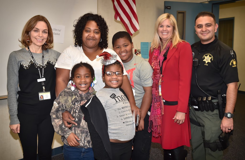 The Thompson family with mom and kids Daleena, 7, Kayla, 5, and 5th grader David pose with TIP volunteer Karolina Lorry, left, San Joaquin Elementary Principal Karen Schibler and OCSD Dep. Anthony Sambrano, right, after David earned a $500 holiday gift for himself and his family from an anonymous donor as part of Operation Secret Santa. Photo by Steven Georges/Behind the Badge OC