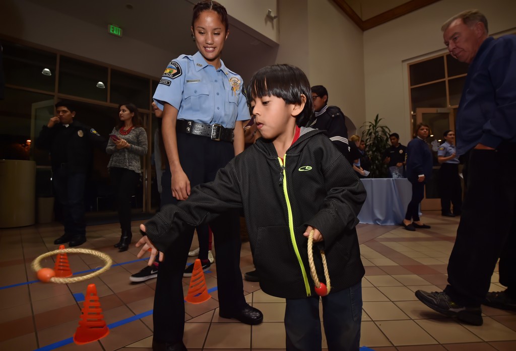 Five-year-old Christian Hernandez tosses a ring in a carnaval booth run by Tustin Explorer Marleen Ramirez during Tustin PD’s annual Santa Cop event for local families. Photo by Steven Georges/Behind the Badge OC