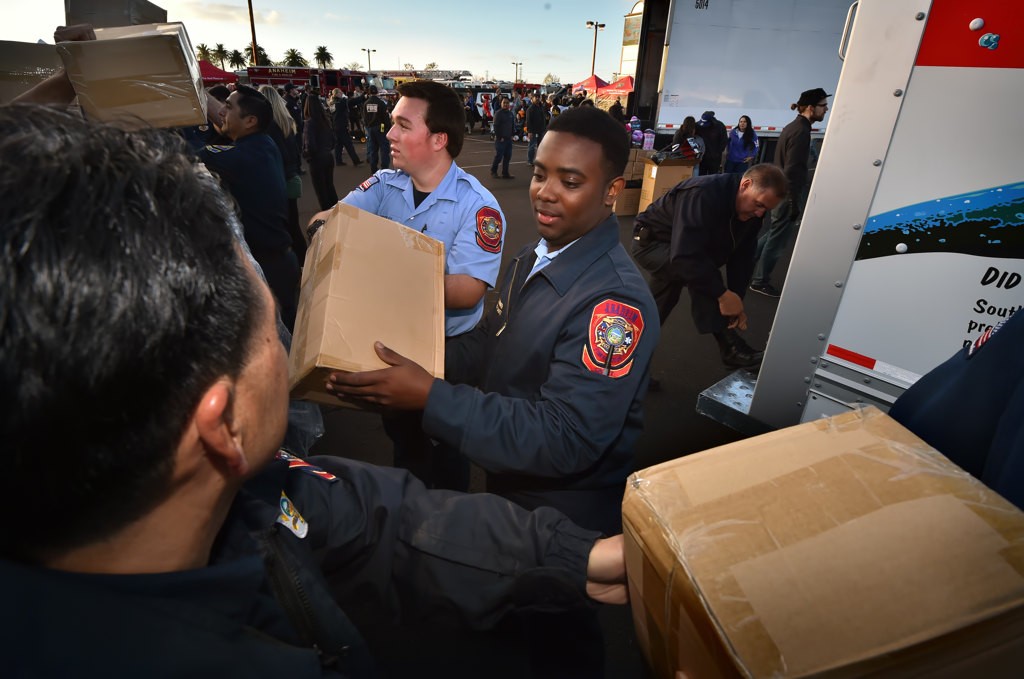 Anaheim Fire & Rescue Cadet Isaiah Turner, center, helps other firefighters move boxes of toys during the Spark of Love Toy Drive at the Honda Center. Photo by Steven Georges/Behind the Badge OC