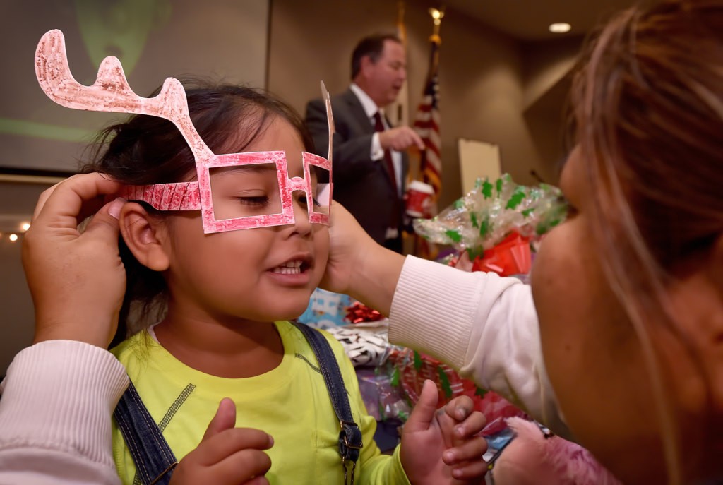 Jocelyn Noriega, 5, has her mother put on the arts and craft reindeer glasses she made as her family gathered for the OCFJC Adopt A Family event. Photo by Steven Georges/Behind the Badge OC