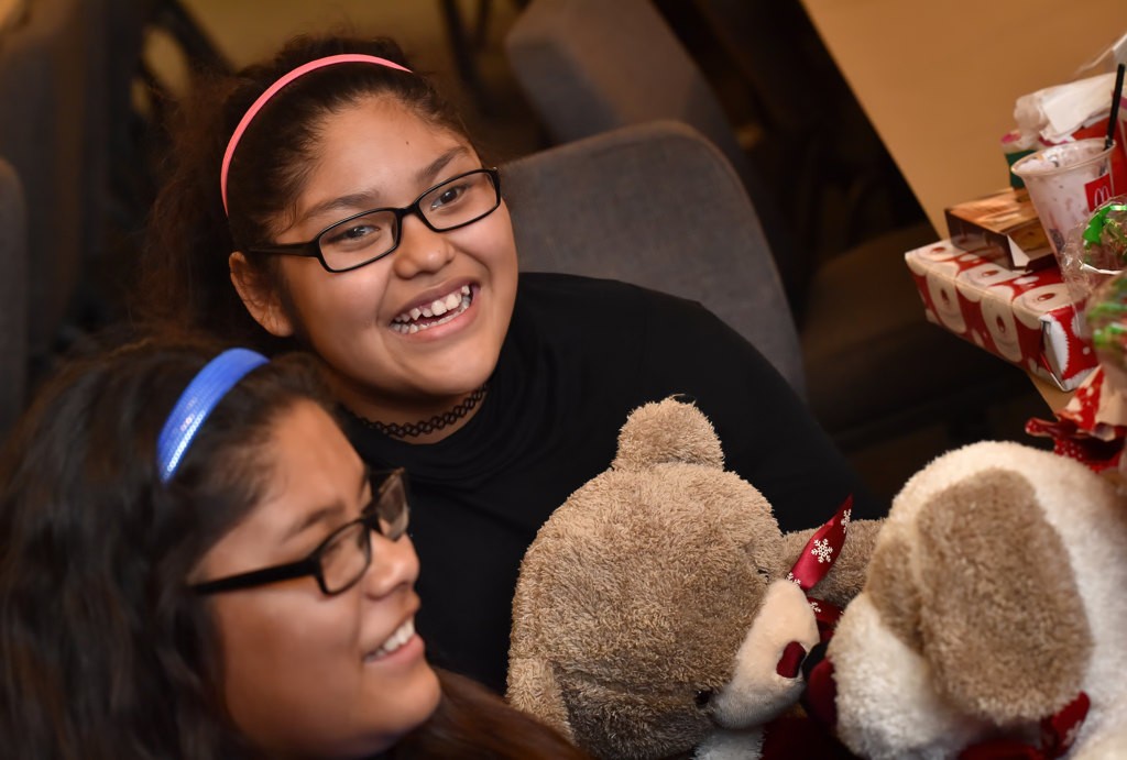 Jennifer Noriega, 11, left, and her sister Nayeli Noriega, 12, smile as they talk about the Christmas gifts they received, including the plush teddy bear and dog, during the OCFJC Adopt A Family event. Photo by Steven Georges/Behind the Badge OC