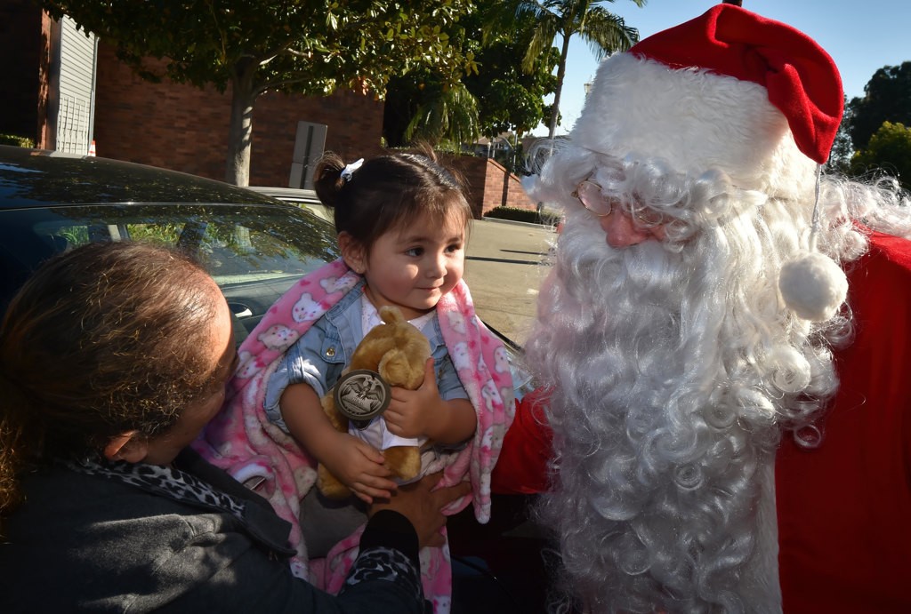One-year-old Aylin of Anaheim smiles as she receives a Teddy Bear from Santa as she visits the Anaheim PD car seat inspection station. Photo by Steven Georges/Behind the Badge OC