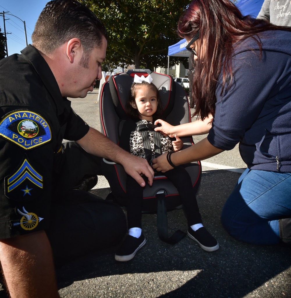 Anaheim Police Officer Eric Anderson has Luna tryout her new car seat before installing it the car. Her old car seat was about to expire qualifying her for a brand new car seat. Photo by Steven Georges/Behind the Badge OC