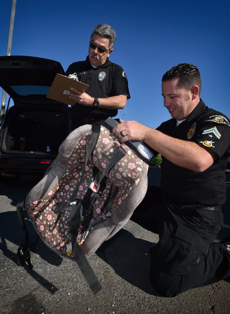 Anaheim PD officers Oscar Ayon, left, and Steve Anderson inspect a car seat at the Anaheim PDÕs car seat inspection station. The car seat was found to have an expiration date of December 2016 qualifying the owner for a new replacement car seat. Photo by Steven Georges/Behind the Badge OC