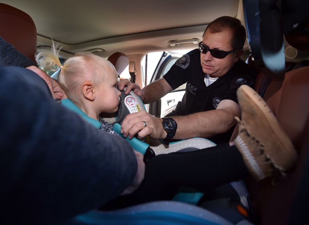 Anaheim PD Officer Steve Anderson helps makes sure 2-year-old Emma SchweringÕs car seat is installed properly at the APD car seat inspection station. Photo by Steven Georges/Behind the Badge OC