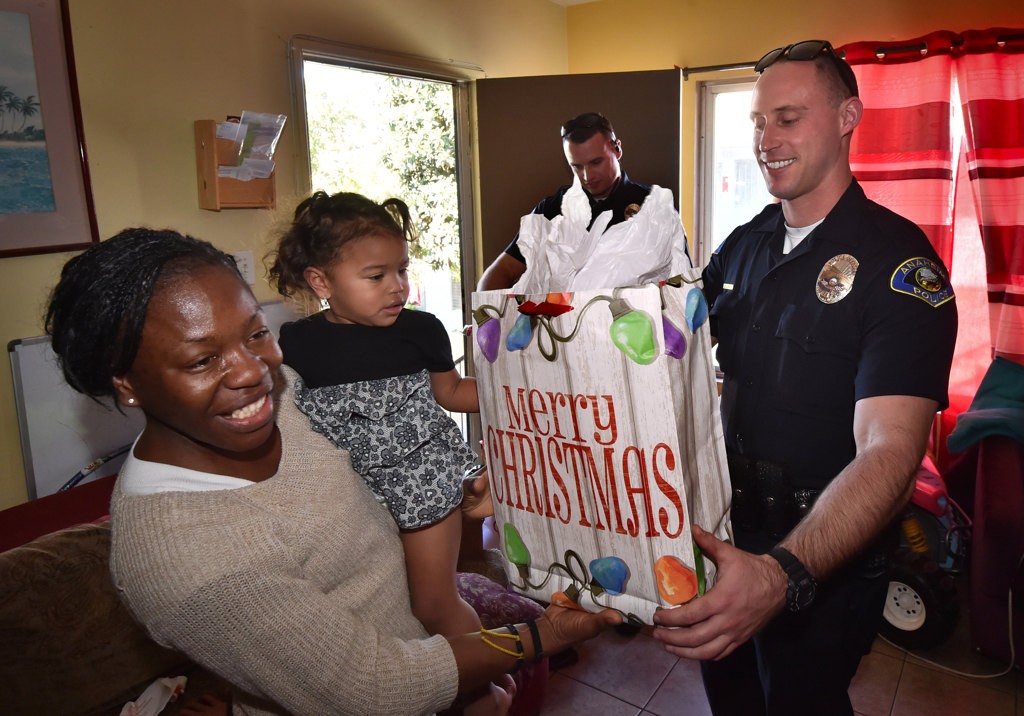 Yensy Flores and her 18-month-old daughter Nanigui Flores receive Christmas gifts from Anaheim PD Officer Brendan Thomas as part of Anaheim PD’s Cops 4 Kids Christmas Delivery. Photo by Steven Georges/Behind the Badge OC