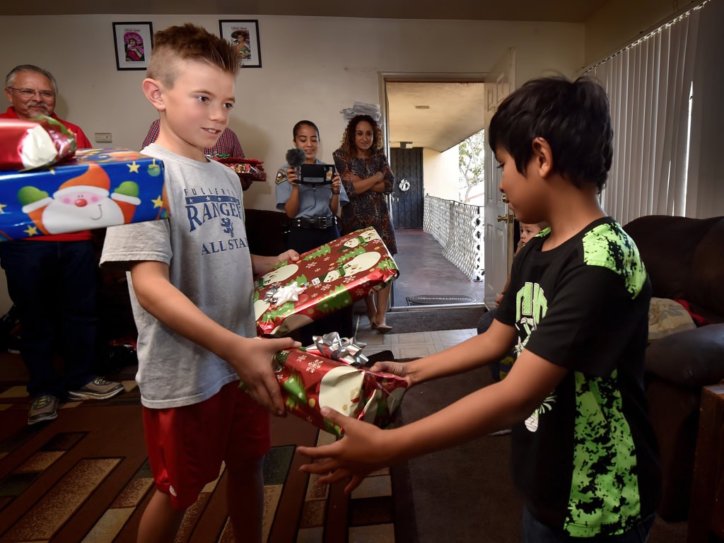 Volunteer Declan Fitzgerald, 8, left, hands out Christmas gifts to Antonio Lemus, 7, as part of Anaheim PD’s Cops 4 Kids Christmas Delivery. Declan is the son of an APD dispatcher. Photo by Steven Georges/Behind the Badge OC