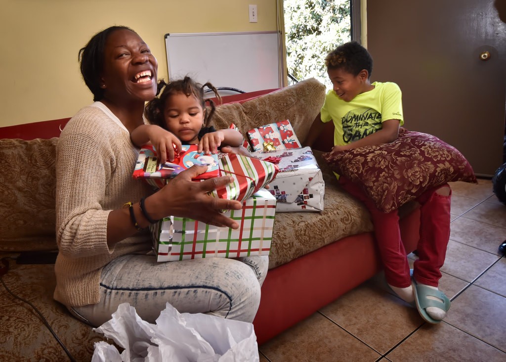 Yensy Flores flashes a big smile as 18-month-old daughter Nanigui Flores and Joshua Rodriguez, 9, open early Christmas gifts from Anaheim PD and Cops 4 Kids. Photo by Steven Georges/Behind the Badge OC
