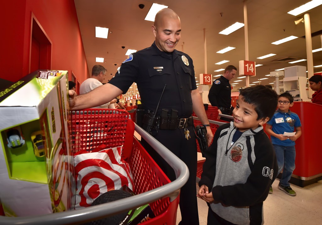 Garden Grove PD Officer Michael Elhami stands with a smiling Andrew Guerra, 8, after helping him out with his shopping choices during the department’s Shop with a Cop. Photo by Steven Georges/Behind the Badge OC