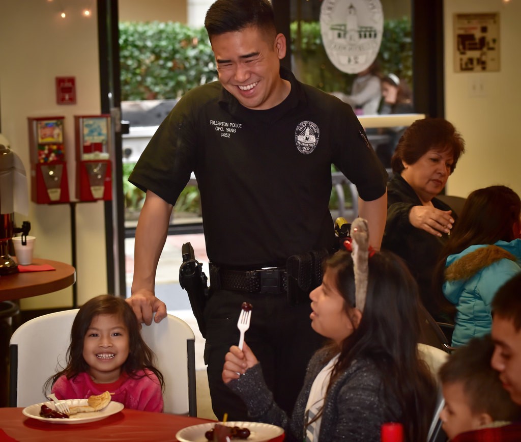 Fullerton PD Officer Michael Yang talks to the kids as they consume their pancake breakfast during the police department’s Adopt a Family holiday program. Photo by Steven Georges/Behind the Badge OC