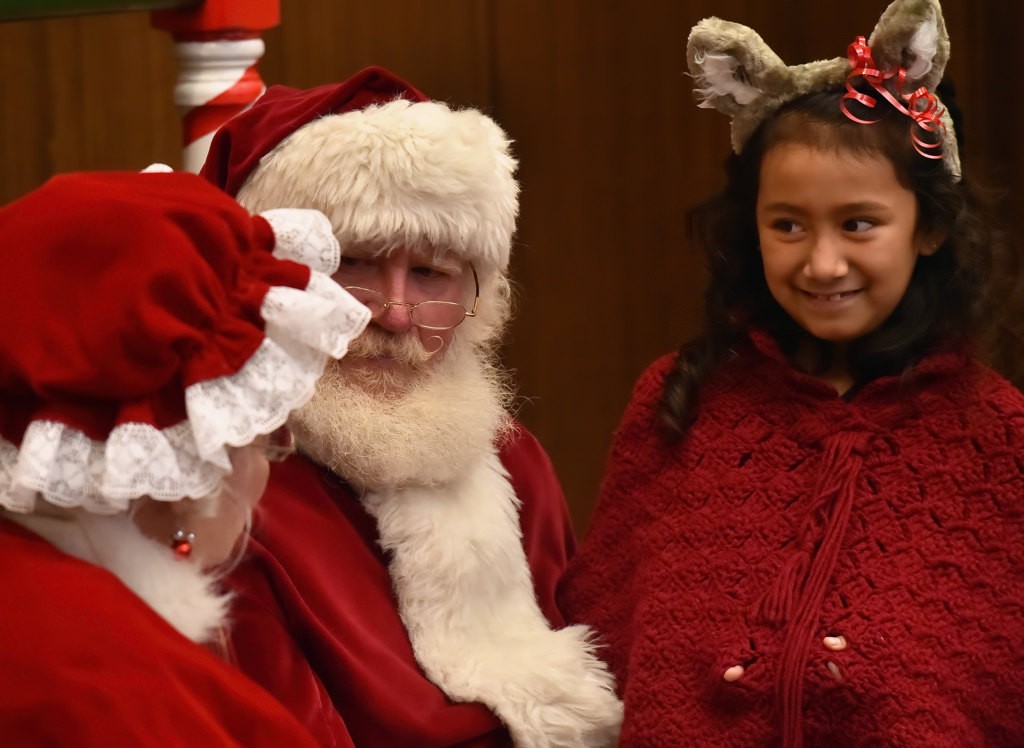 Evelyn Corral, 8, smiles as Santa and Mrs. Claus talk to children during Fullerton PD”s Adopt a Family holiday program. Photo by Steven Georges/Behind the Badge OC