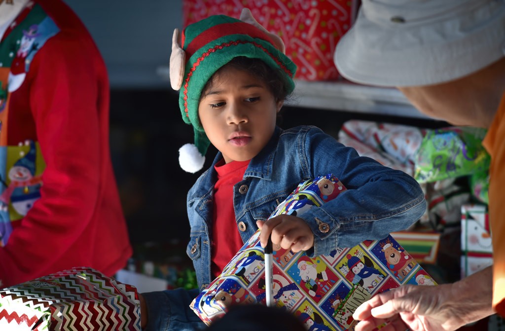 Jazmyn Fuller, 7, who’s mother works with St. Joseph Medical Group, volunteers her time on Christmas Eve morning to hand out presents during Anaheim’s Community Holiday Brunch. Photo by Steven Georges/Behind the Badge OC
