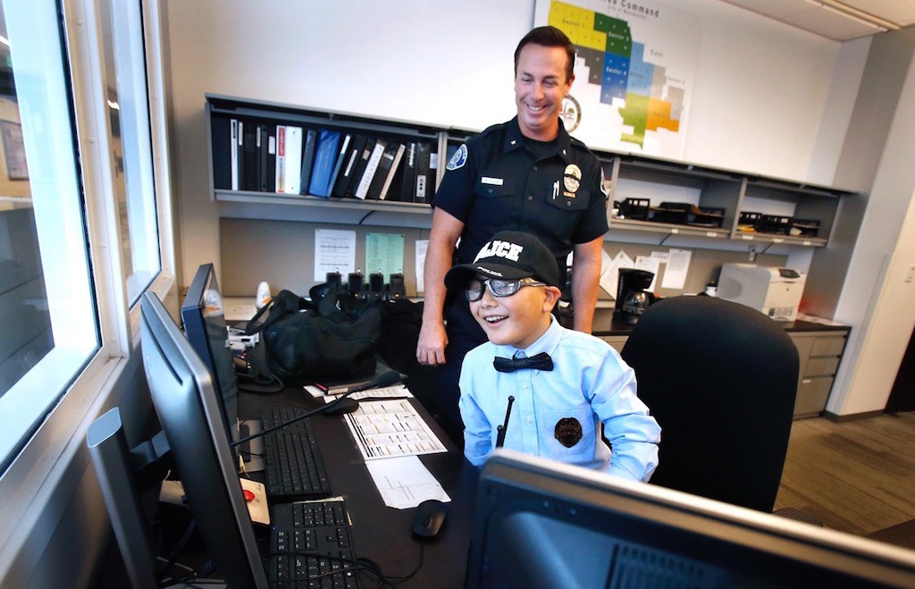 Mateo Sanchez, 9, takes a seat in the Watch Commander's chair as Cmdr. Bill Collins looks on. Photo by Christine Cotter/Behind the Badge OC. 