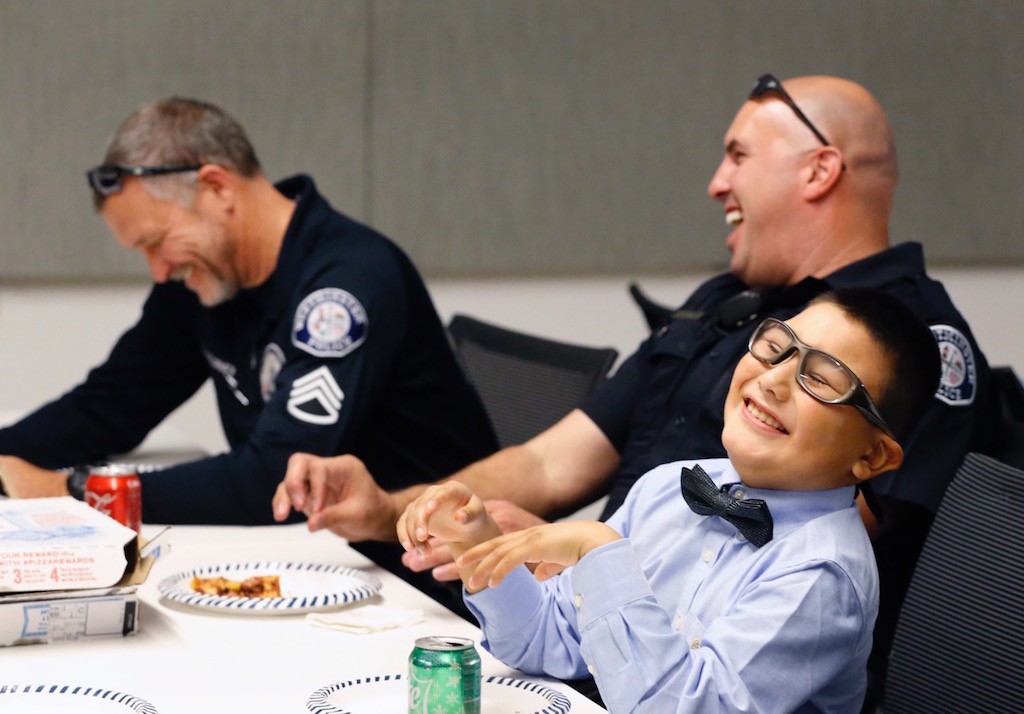 Sgt. Kevin MacCormick, Officer Roland Perez and Mateo Sanchez share a laugh over pizza. Photo by Christine Cotter/Behind the Badge OC. 