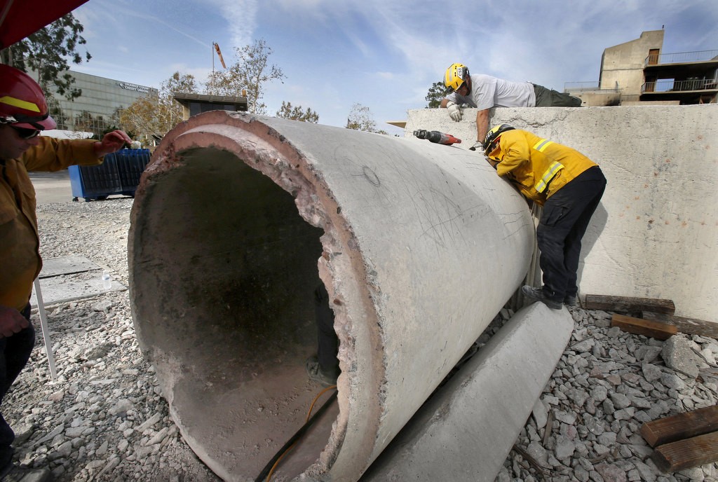 Wade Haller, top, assists as a fellow firefighter inside a concrete pipe uses a core drill to cut through a thick concrete wall. Photo by Christine Cotter