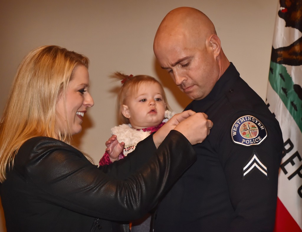 Cpl. Michael Harvey gets his new badge pinned to him by his wife, Wendy Harvey, while holding his 15-month-old daughter Reese, during a Westminster PD promotion ceremony. Photo by Steven Georges/Behind the Badge OC