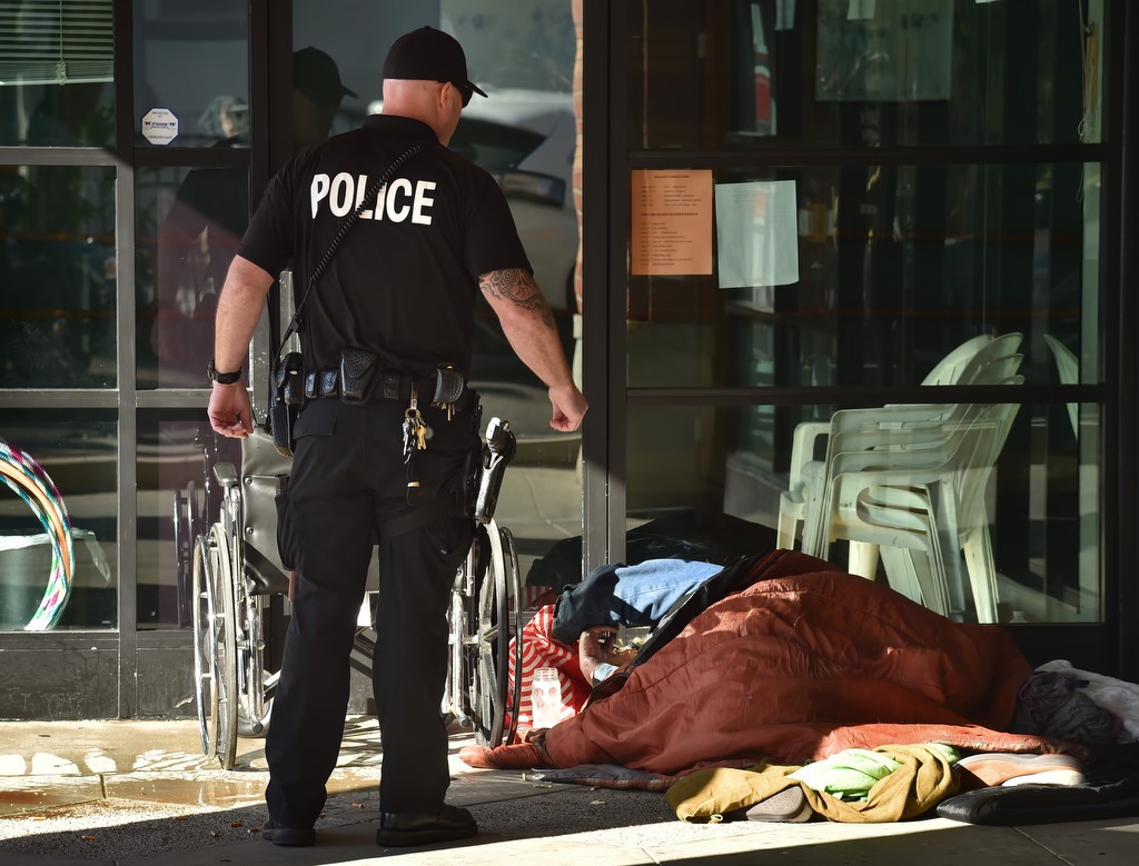 Cpl. Dan Heying, of the Fullerton PD Homeless Liaison Unit, talks to a homeless man sleeping in front of the entrance to a business on Wilshire Ave. in Fullerton. Photo by Steven Georges/Behind the Badge OC