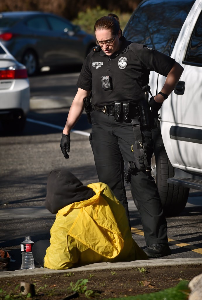 Cpl. Ginny Johnson of the Homeless Liaison Unit talks to a homeless man camped out with his belongings in a business parking lot. Photo by Steven Georges/Behind the Badge OC