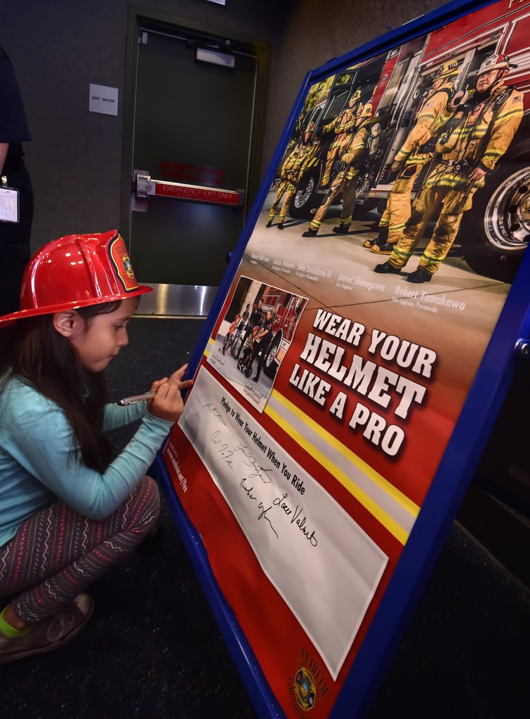 Alexis Toro, 5, signs a pledge to “Wear Your Helmet When You Ride” during a talk at the Anaheim Library. Kids at the event who signed the pledge received a free bicycle helmet (in addition to the fire helmet) from Anaheim Fire & Rescue. Photo by Steven Georges/Behind the Badge OC