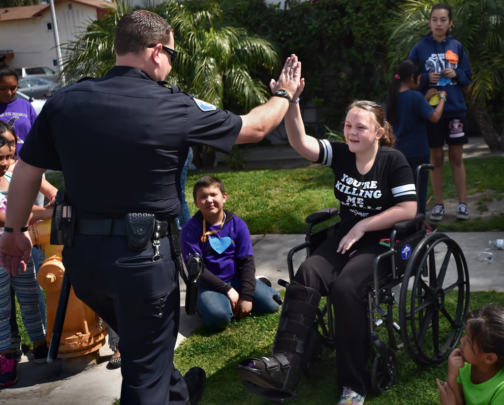 Garden Grove PD Officer Taylor Macy gets a high-five from 12-year-old Erin Rose Hardin as kids gather at the Palma Vista neighborhood to meet two GGPD officers. Photo by Steven Georges/Behind the Badge OC