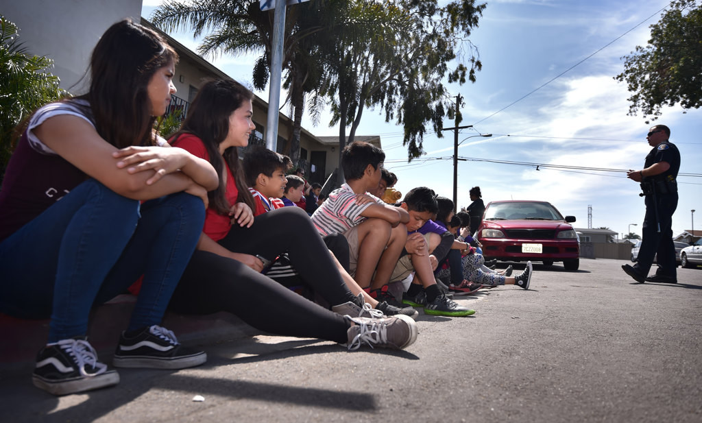 Kids from the Palma Vista neighborhood in Garden Grove listen to GGPD Officer Taylor Macy as they gather for the Junior Neighborhood Watch Club kick-off event. Photo by Steven Georges/Behind the Badge OC